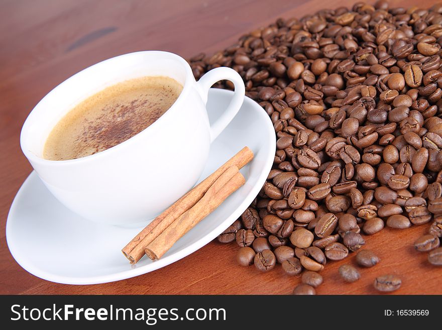 Cup of coffee sprinkled with cinnamon and with cinnamon sticks and coffee beans on a wooden table
