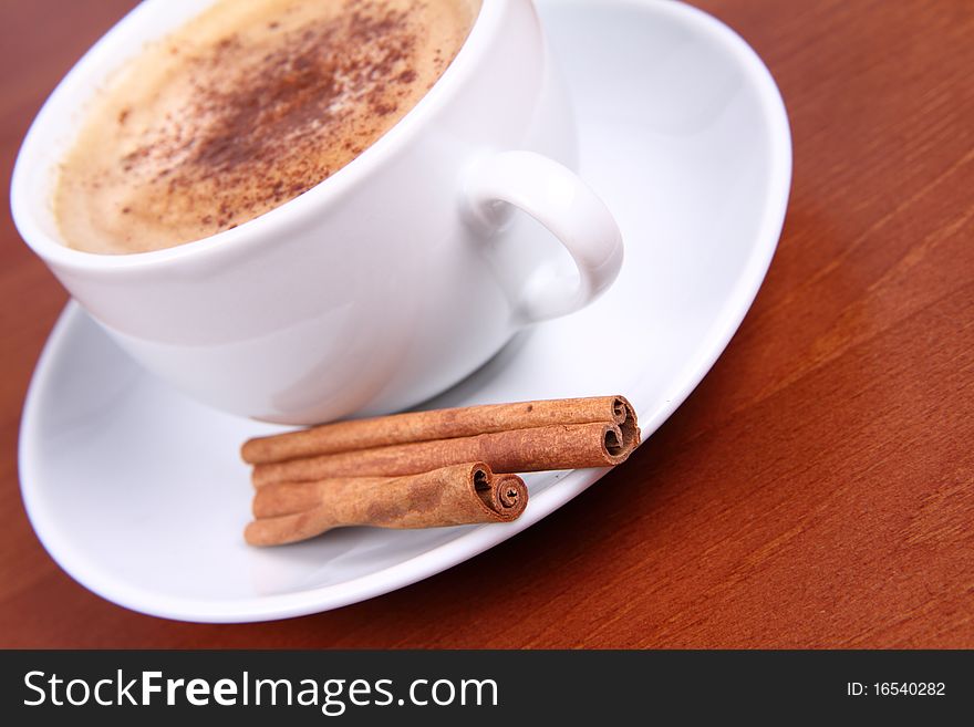 Cup of coffee sprinkled with cinnamon and with cinnamon sticks on wooden background