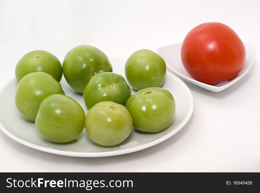 Green and red tomatos on a plate on a white background closeup