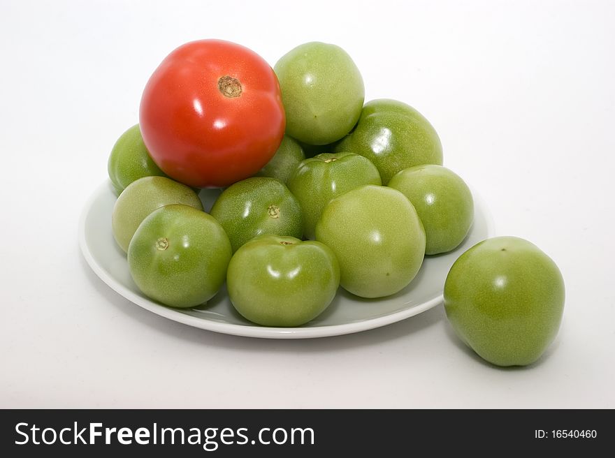 Green and red tomatos on a plate on a white background closeup