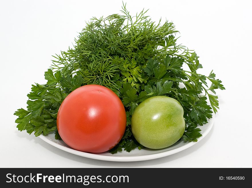 Green and red tomatos and fresh herbs on a plate on a white background closeup