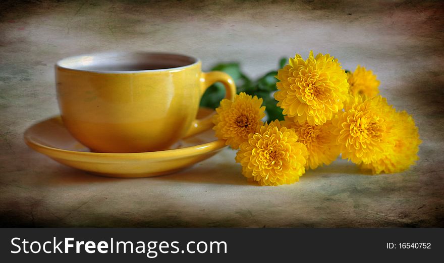 Yellow cup with tea, alongside yellow chrysanthemums. Yellow cup with tea, alongside yellow chrysanthemums