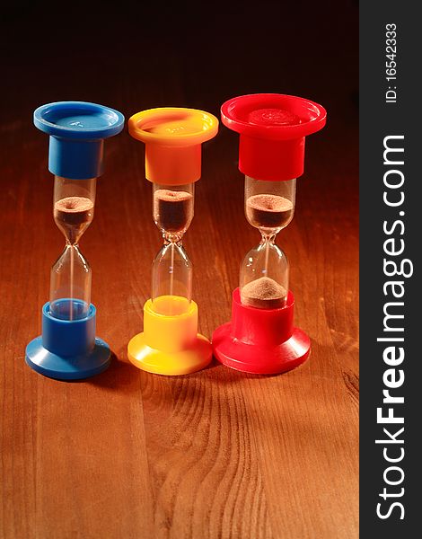 Three colored hourglasses standing on wooden background. Three colored hourglasses standing on wooden background