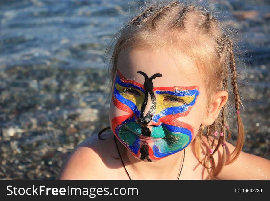Child's face painted as butterfly at the seaside