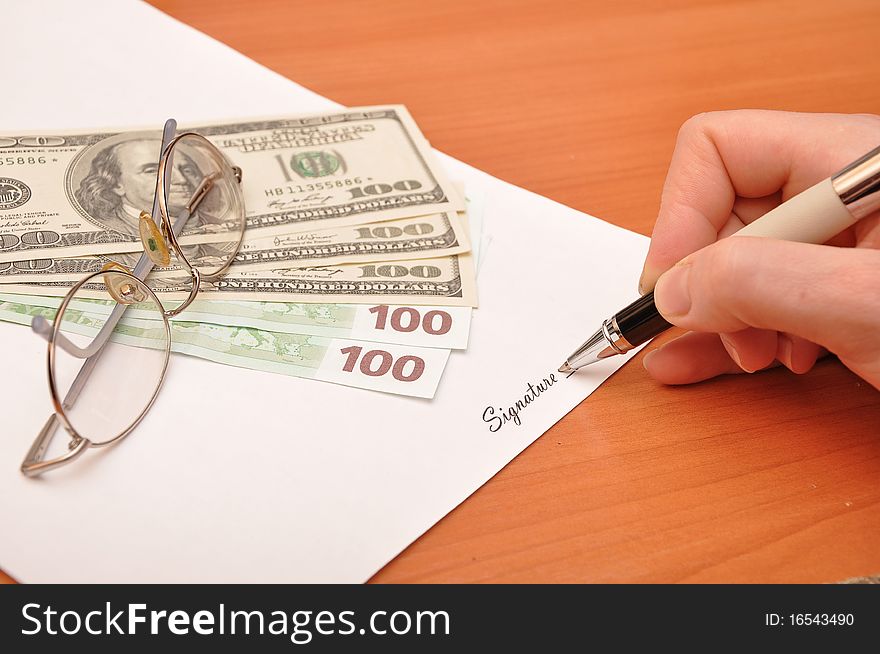 Hand is signing the business document near money. Hand is signing the business document near money