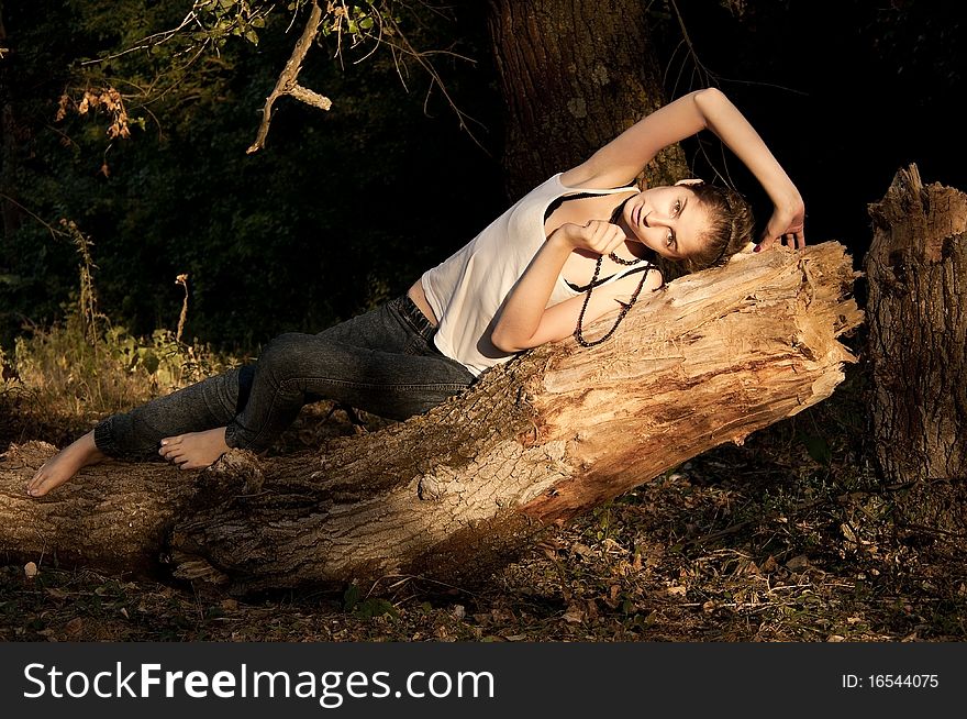 Young girl in jeans and a white T-shirt lying on a fallen tree in  forest. Young girl in jeans and a white T-shirt lying on a fallen tree in  forest