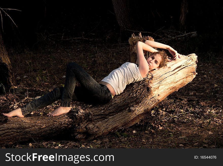 Young girl in jeans and a white T-shirt lying on a fallen tree in  forest. Young girl in jeans and a white T-shirt lying on a fallen tree in  forest