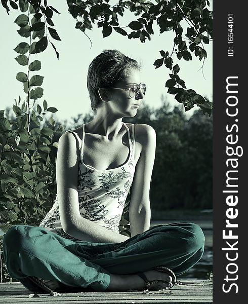 Young woman in sunglasses sitting in lotus position on the background of lakes and forests. monochrome. cold tone. Young woman in sunglasses sitting in lotus position on the background of lakes and forests. monochrome. cold tone.