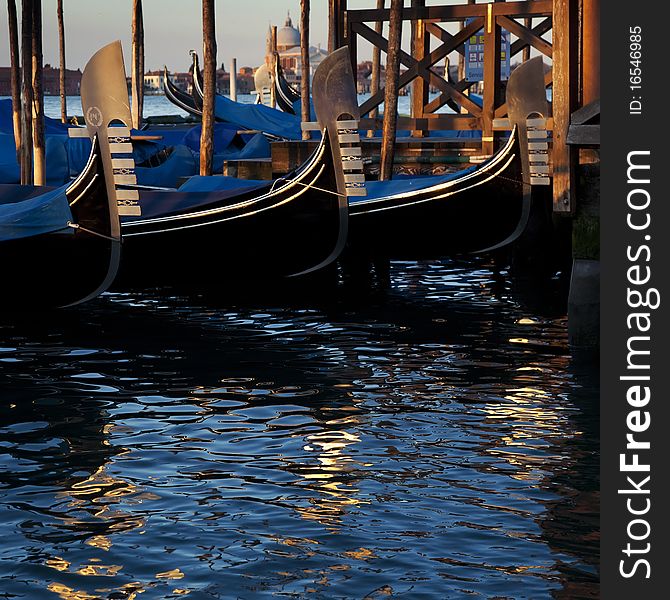 Noses of three gondolas in the dock of Venice. Bright reflections if water.