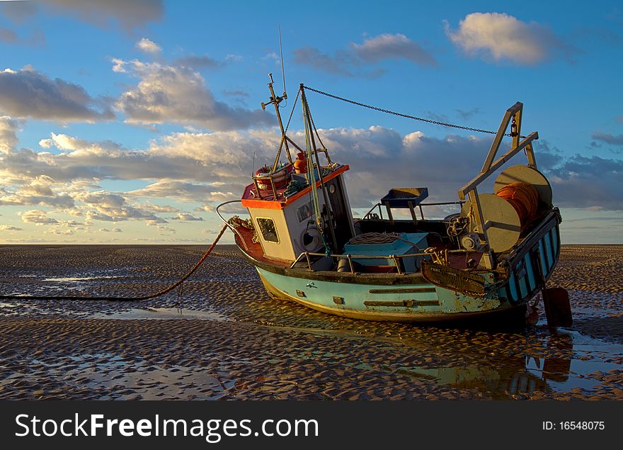 A small blue trawler resting on muddy beach near sunset - HDR image brightly coloured. A small blue trawler resting on muddy beach near sunset - HDR image brightly coloured