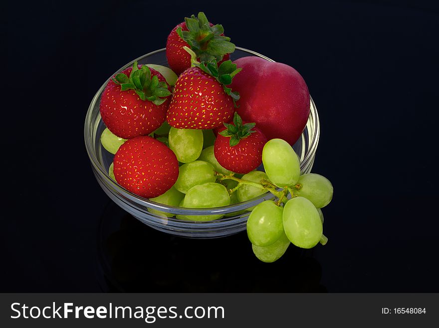 Strawberries and grapes in a glass bowl on a black background. Strawberries and grapes in a glass bowl on a black background
