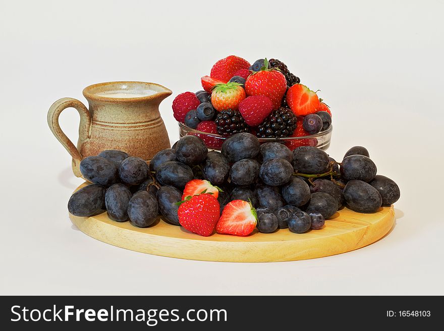 Strawberries and grapes and other soft fruit on a wooden platter with cream jug. Strawberries and grapes and other soft fruit on a wooden platter with cream jug