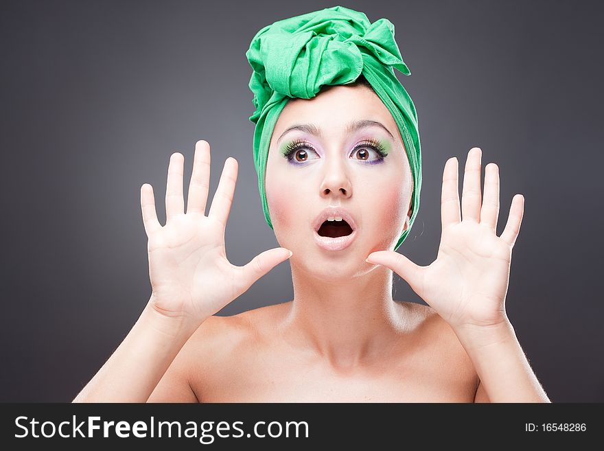 Surprised excited woman with pink-green makeup in green hat with open mouth