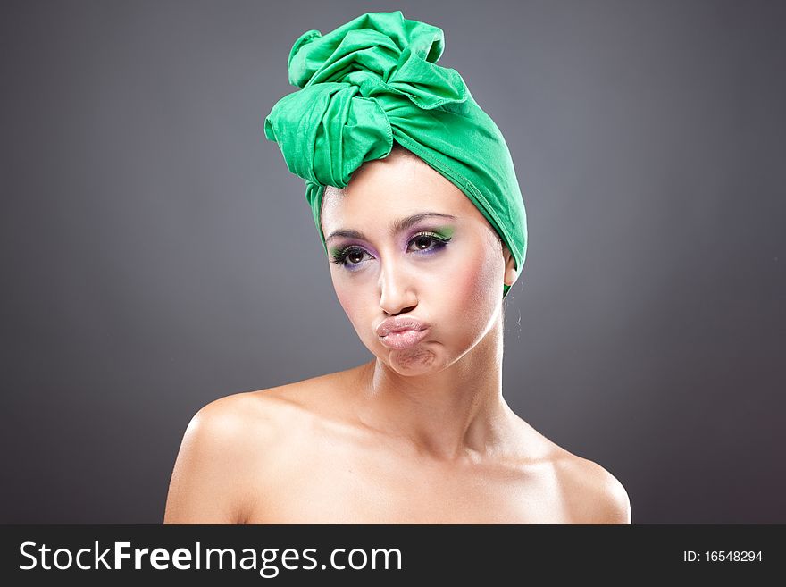 Upset young woman with pink-green makeup in green hat