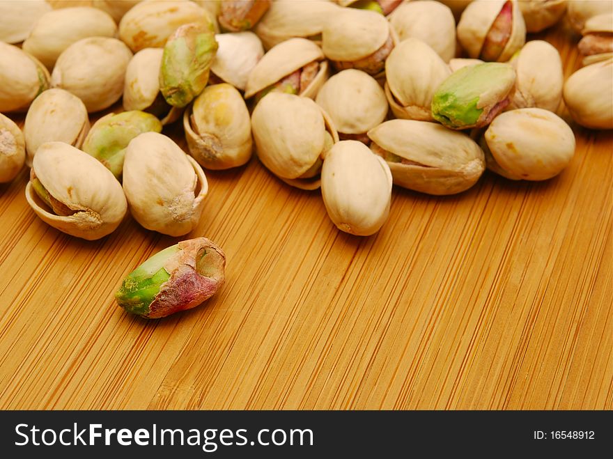 Pile of salted green pistachio  nuts on wooden board. Pile of salted green pistachio  nuts on wooden board