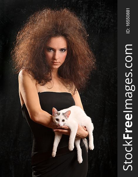 Portrait of the beautiful young woman with a magnificent hairdress And the WHITE CAT ON the SHOULDER on a black background.