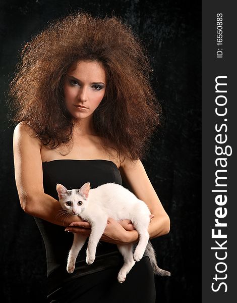 Portrait of the beautiful young woman with a magnificent hairdress And the WHITE CAT ON the SHOULDER on a black background.