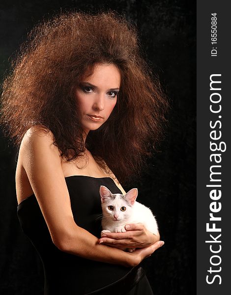 Portrait of the beautiful young woman with a magnificent hairdress And the WHITE CAT ON the SHOULDER on a black background.