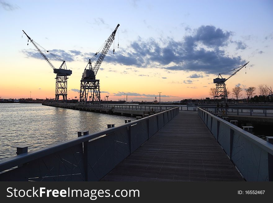 Three cranes and a boardwalk pier silhouetted against the sunset in the harbor at Erie Basin Park at Red Hook Brooklyn - Brooklyn, NY. Three cranes and a boardwalk pier silhouetted against the sunset in the harbor at Erie Basin Park at Red Hook Brooklyn - Brooklyn, NY
