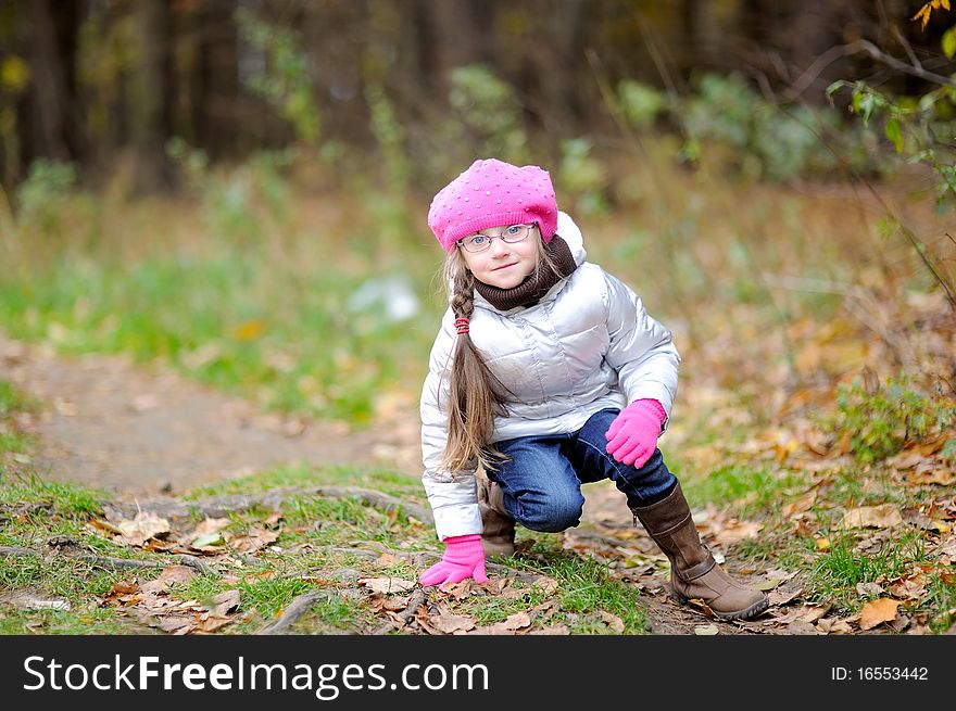 Adorable small girl in bright pink hat with long dark hair and glasses on beauty late autumn background