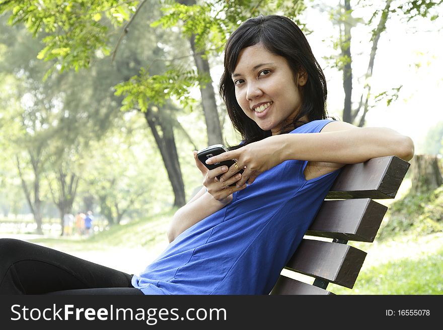 A smiling Asian woman using her cellphone on a park bench. A smiling Asian woman using her cellphone on a park bench