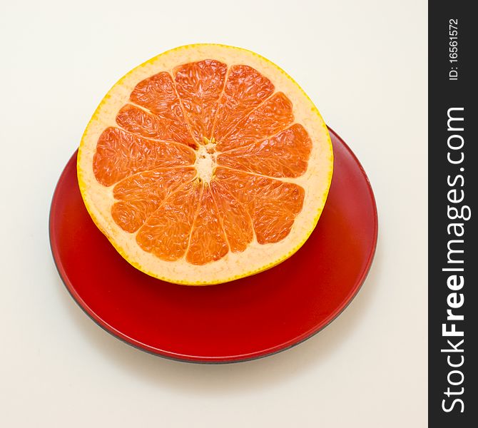 Half a grapefruit is on a brown dish and the dish is on a white background. Half a grapefruit is on a brown dish and the dish is on a white background.