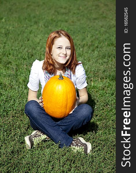 Young women sitting at green grass and keeping pumpkin.