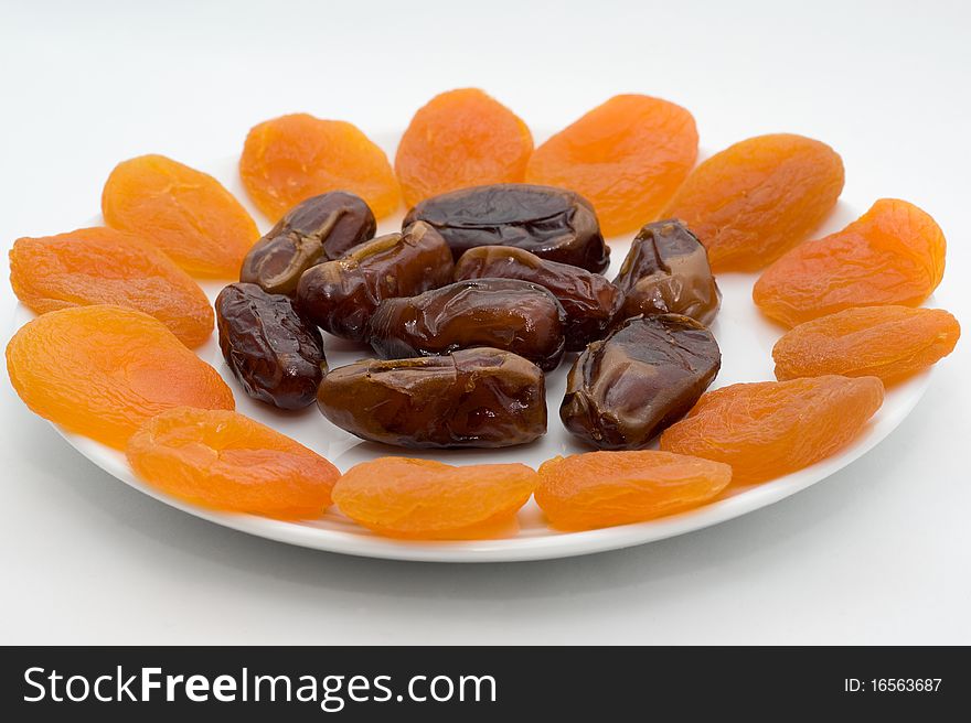 The fruits of the Phoenix and dried apricots on a plate on a white background