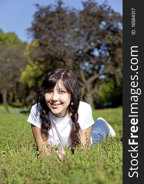 Portrait of beautiful brunette girl with blue eyes on green grass in the park.