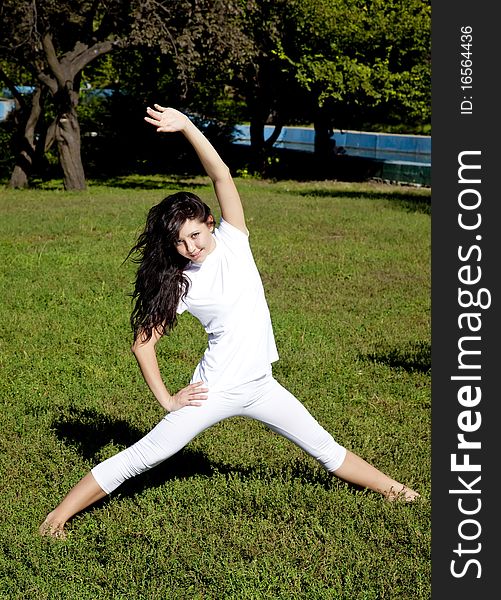 Beautiful young brunet yoga girl on green grass in park.