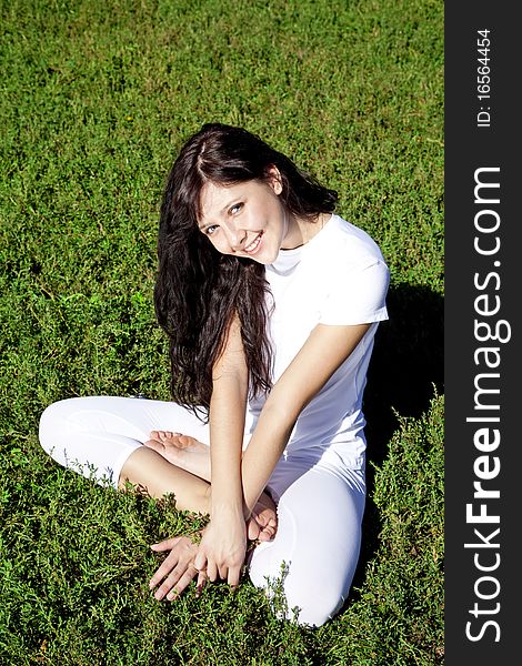 Brunet yoga girl on green grass in park.