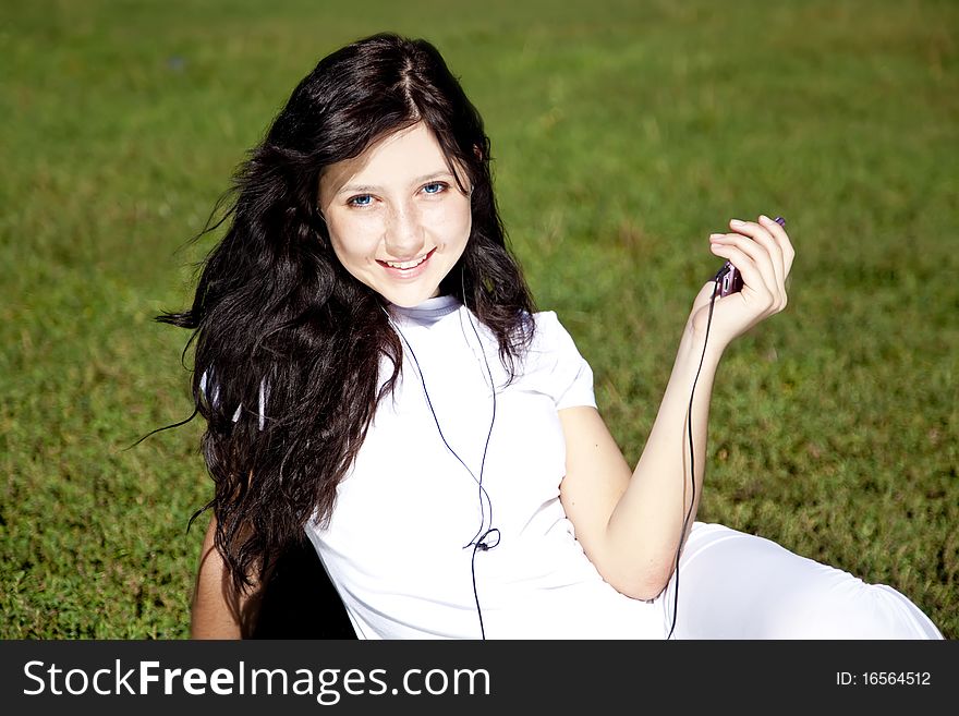 Pretty young brunette girl listening music on green grass in the park and show pink music player. Pretty young brunette girl listening music on green grass in the park and show pink music player.