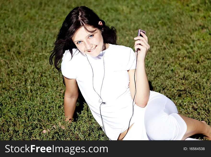 Pretty young brunette girl listening music on green grass in the park and show pink music player. Pretty young brunette girl listening music on green grass in the park and show pink music player.