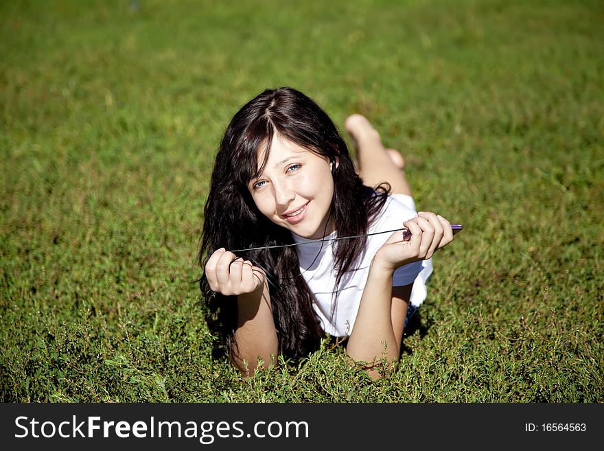Pretty young brunette girl listening music on green grass in the park and show pink music player. Pretty young brunette girl listening music on green grass in the park and show pink music player.