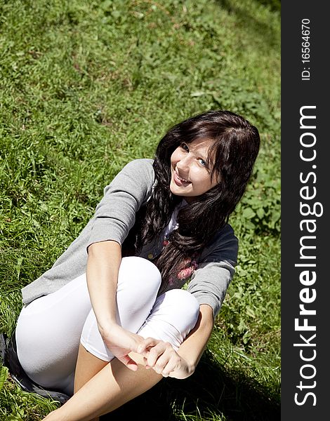 Portrait of beautiful brunette girl with blue eyes on green grass in the park. Portrait of beautiful brunette girl with blue eyes on green grass in the park.