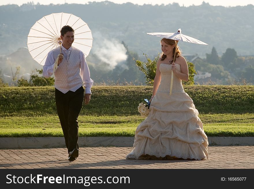 Red head beautiful bride and groom walking outside in sun with umbrellas jumping and smiling