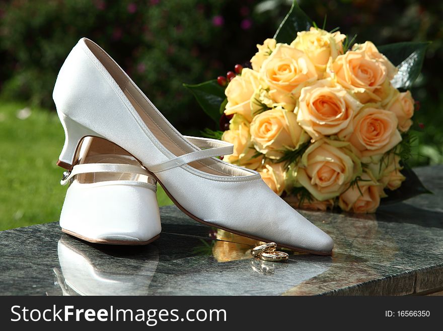 Engagement - shoes with orange rose bouquet and white bridal shoes and golden rings. focus is on rings and shoes. Engagement - shoes with orange rose bouquet and white bridal shoes and golden rings. focus is on rings and shoes