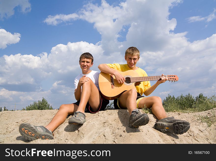 Teenagers play on a guitar sitting on sand. Teenagers play on a guitar sitting on sand
