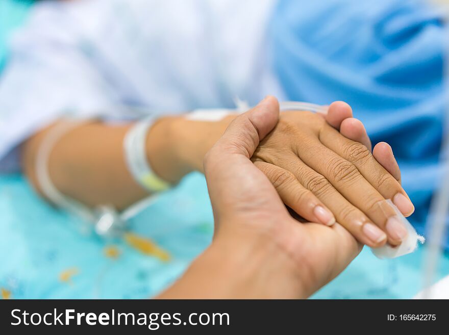 Husband holding wife hand giving normal saline solution or sodium chloride after surgery in hospital.