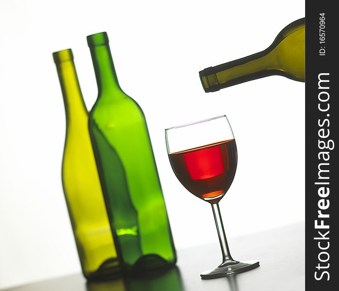Glass of red wine with two green wine bottles