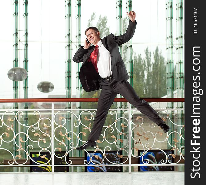 Smiling jumping man with mobile phone on background of glass wall