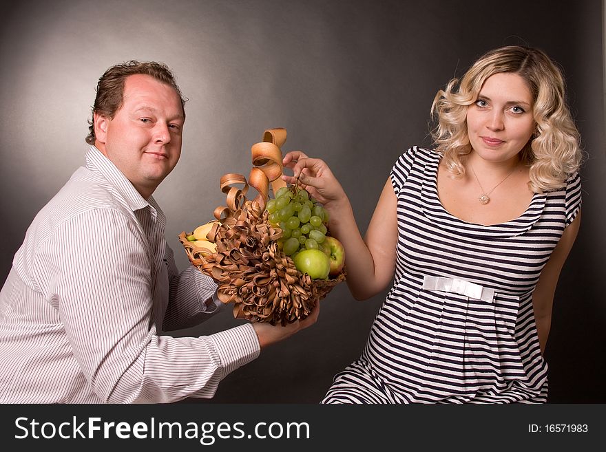 Photo of family pair with the basket of fruit. A woman is pregnant