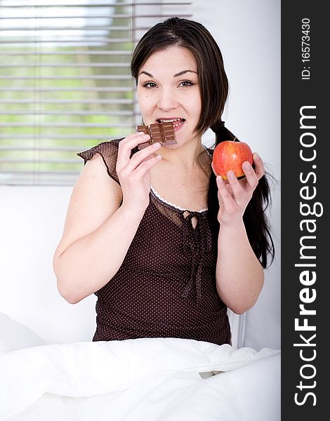 Young adult brunette woman in bed with chocolate and apple