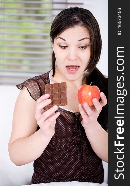 Young adult brunette woman in bed with chocolate and apple