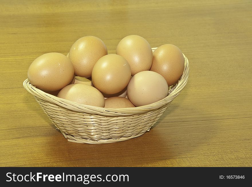 This image shows a wicker basket with chicken eggs on a wooden board. This image shows a wicker basket with chicken eggs on a wooden board