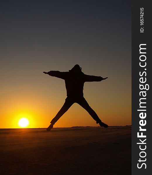 A person jumping in the air during sunset at a beach. A person jumping in the air during sunset at a beach