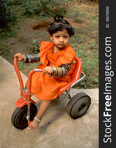 Young Indian girl in orange dress with armful of bangles riding a tricycle. Young Indian girl in orange dress with armful of bangles riding a tricycle