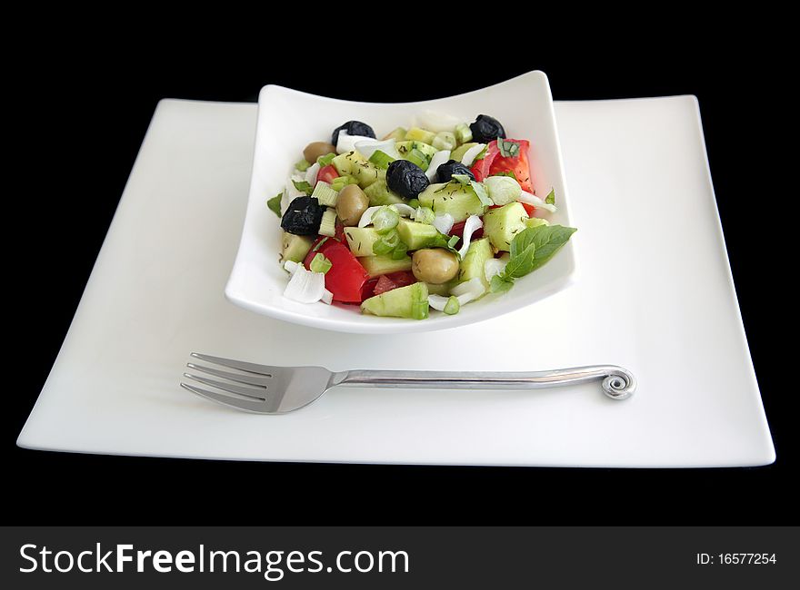 Greek salad (black and green olives, tomato, cucumber, herbs, fresh onion) in white dishware shot on black background.