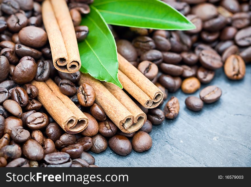 Cinnamon sticks with coffee beans and green leaves on slate background. Cinnamon sticks with coffee beans and green leaves on slate background