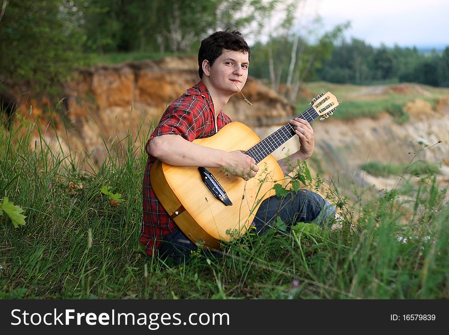 A lone young man with a guitar on a precipice with grass in his mouth. A lone young man with a guitar on a precipice with grass in his mouth